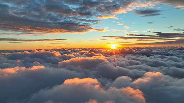 Sun goes into the clouds. Epic sunset in the sky, aerial shot. Flying above the clouds illuminated by the evening sun